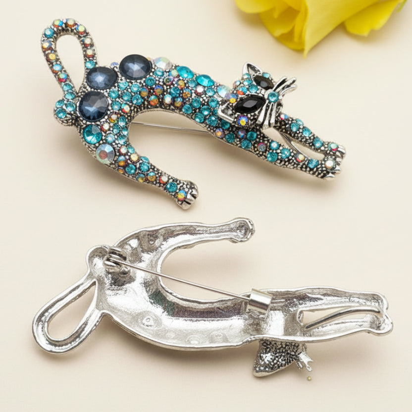 Backside of decorative cat-shaped brooch with colorful blue rhinestones on a light background