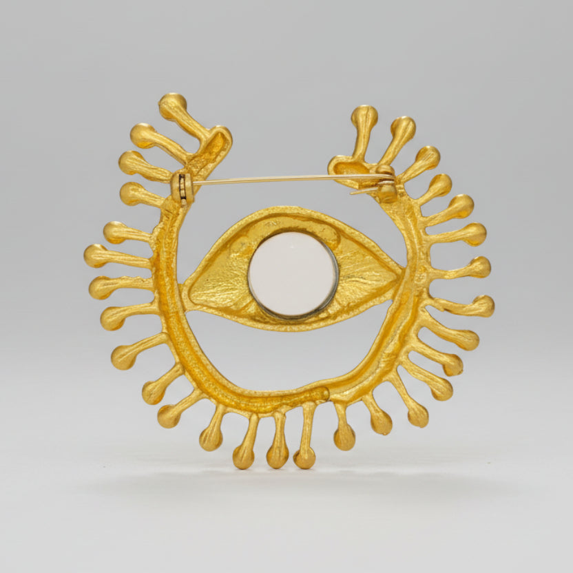 Backside of gold eye-shaped brooch with blue gemstone on a light background