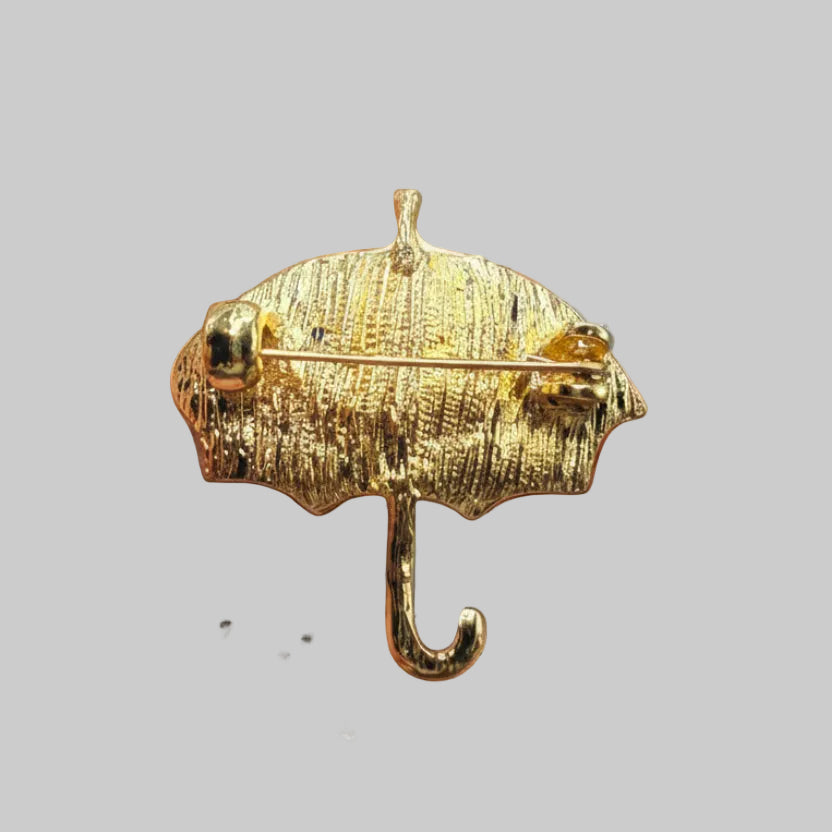 Backside of enamel umbrella brooch with blue and yellow design on a light gray background