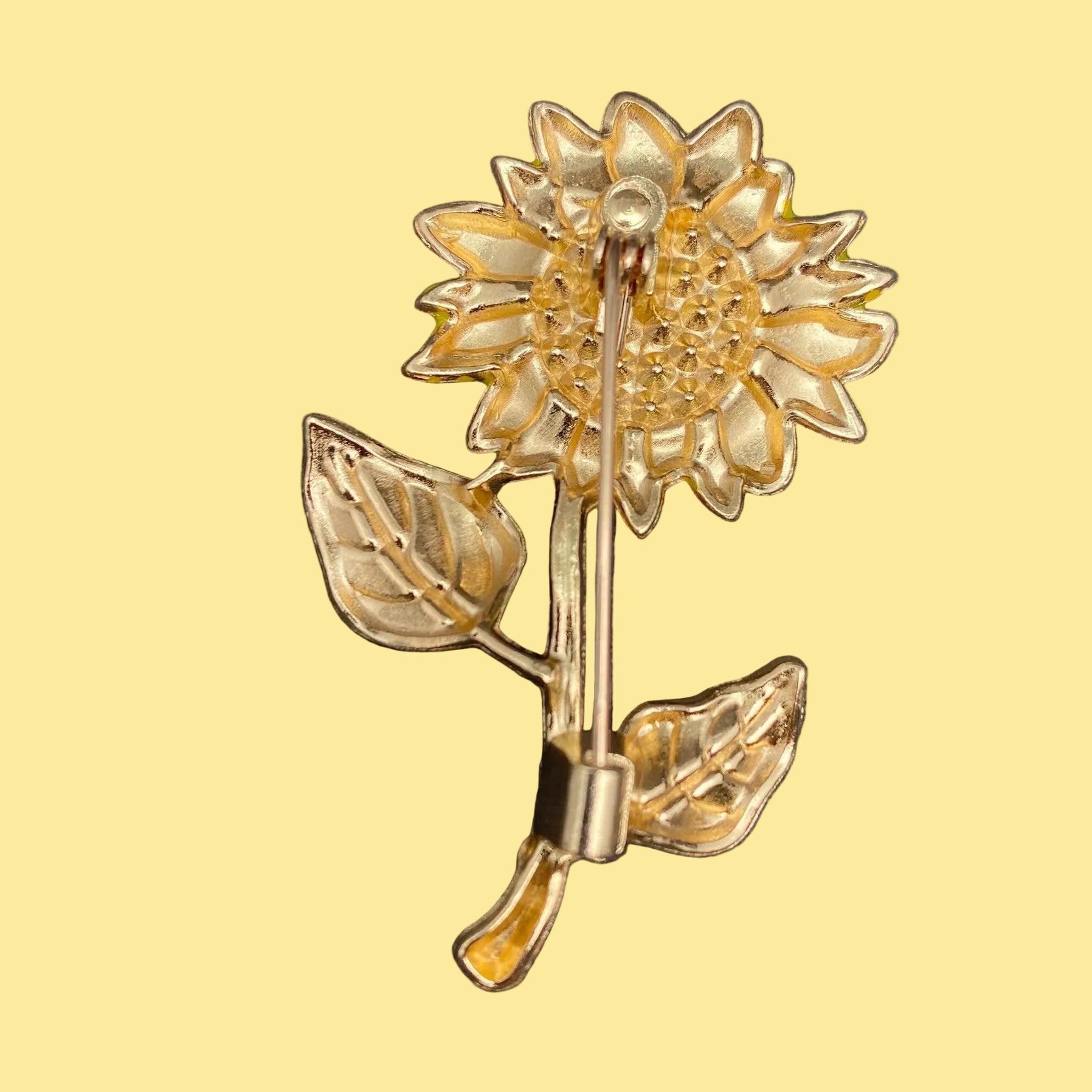 Backside of gold rhinestone sunflower brooch on a pale yellow background