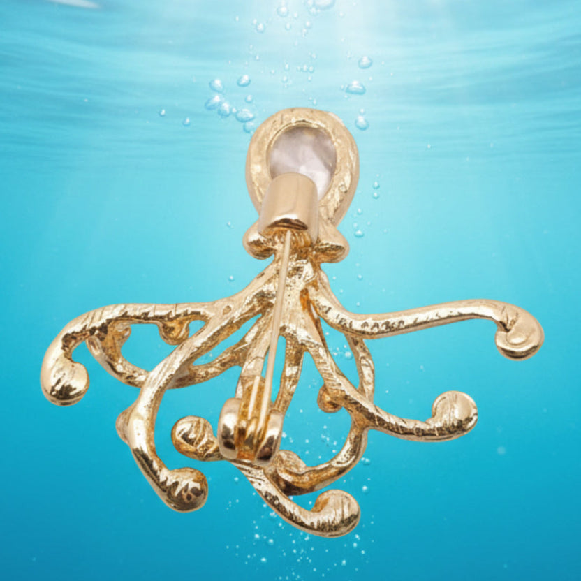 Backside of golden octopus brooch with a red glass head on a underwater background