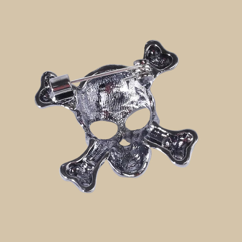 Backside of silver skull and crossbones brooch pin with clear crystal stones on a beige background