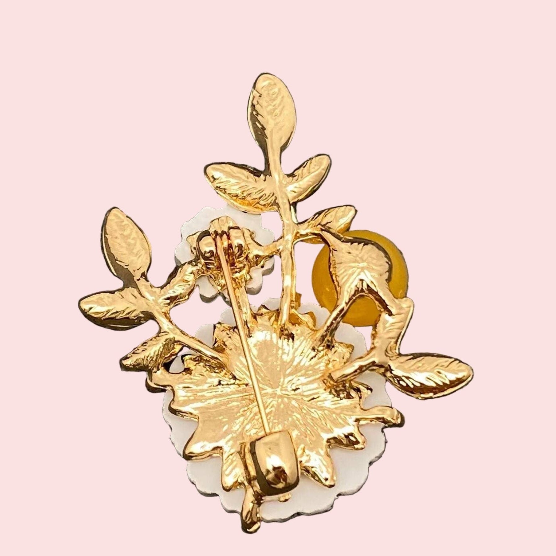 Backside of floral brooch with white flowers, green leaves, and a yellow berry on a pink background