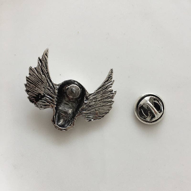 Backside of silver skull brooch with wings on a light gray background