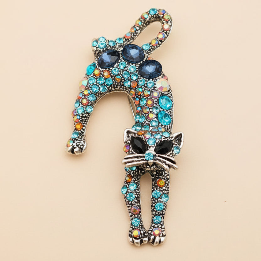 Decorative cat-shaped brooch with colorful blue rhinestones on a light background