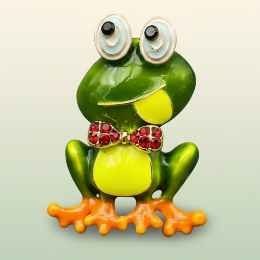 Decorative frog brooch with a red bow tie on a soft white background