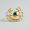 Gold eye-shaped brooch with blue gemstone on a light background