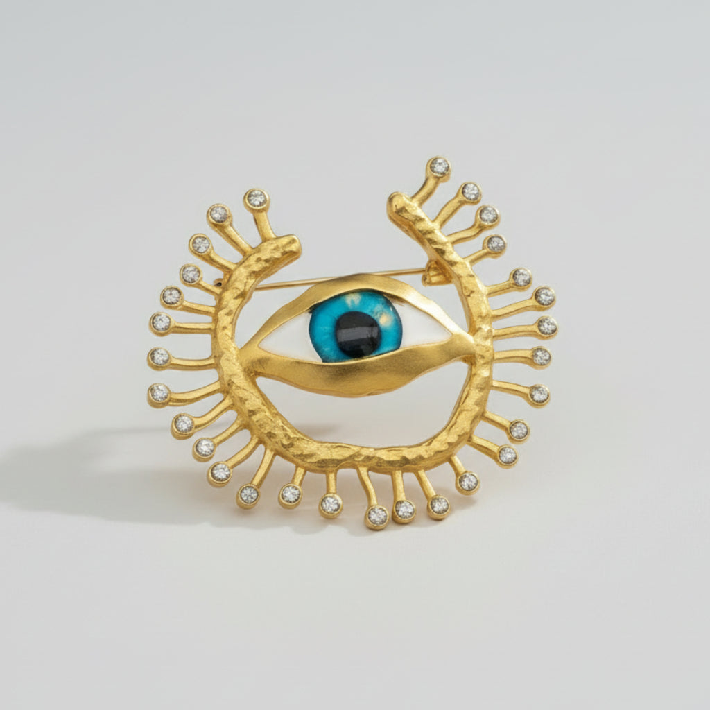 Gold eye-shaped brooch with blue gemstone on a light background