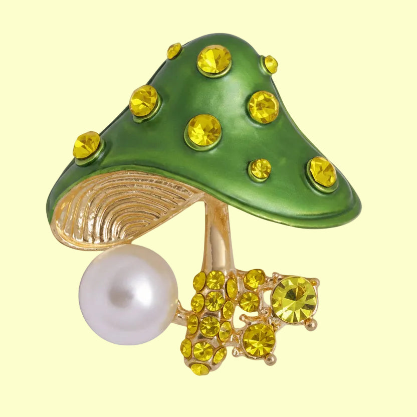 Green top mushroom brooch with yellow gemstones and a faux pearl accent on a soft white background