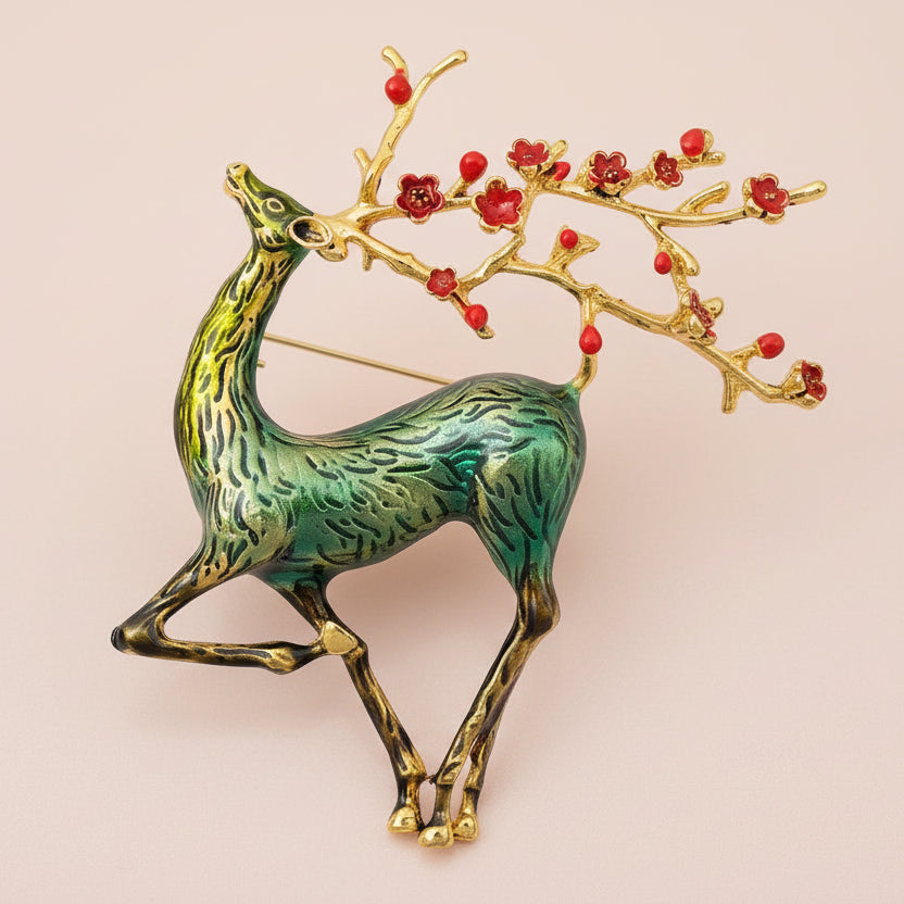 Green sika deer brooch with branch style antlers embellished with red berries on a white background