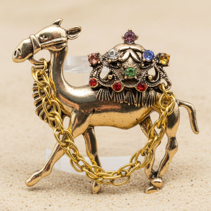 Gold camel brooch with colorful gemstones on a beige background