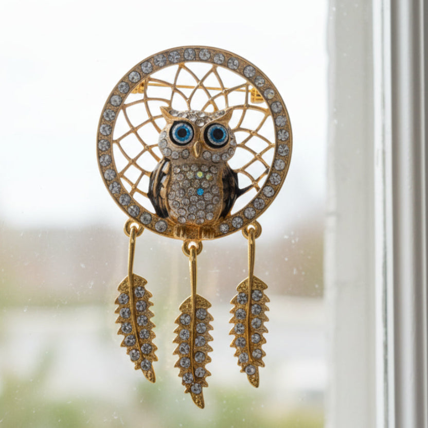Gold dreamcatcher brooch with an owl design on a window background
