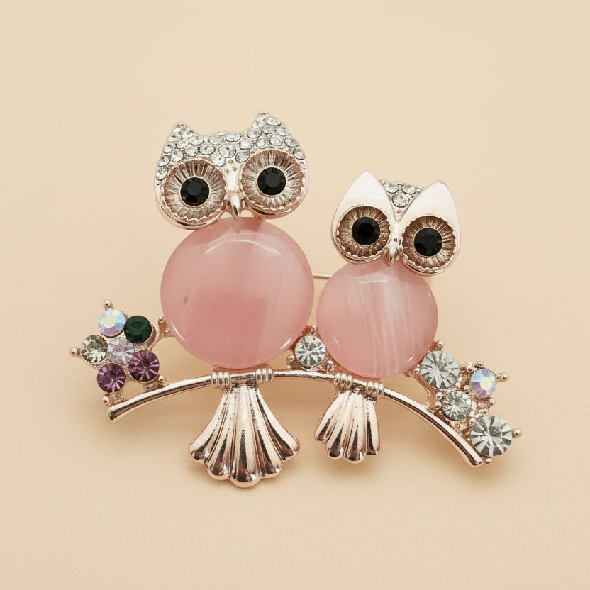 Decorative owl brooch with pink stones on a light pastel peach background