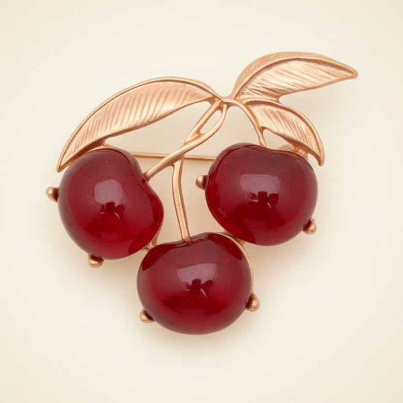 Red lucite triple cherry brooch with gold leaves on a cream background