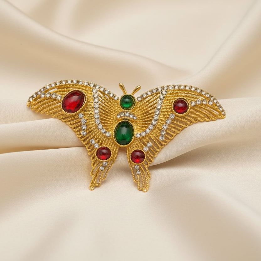 Golden butterfly brooch with red and green gemstones on a cream colored background