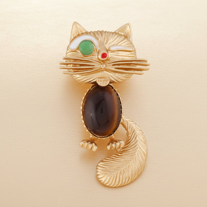 Retro golden cat brooch with a brown catseye stone center on a beige background