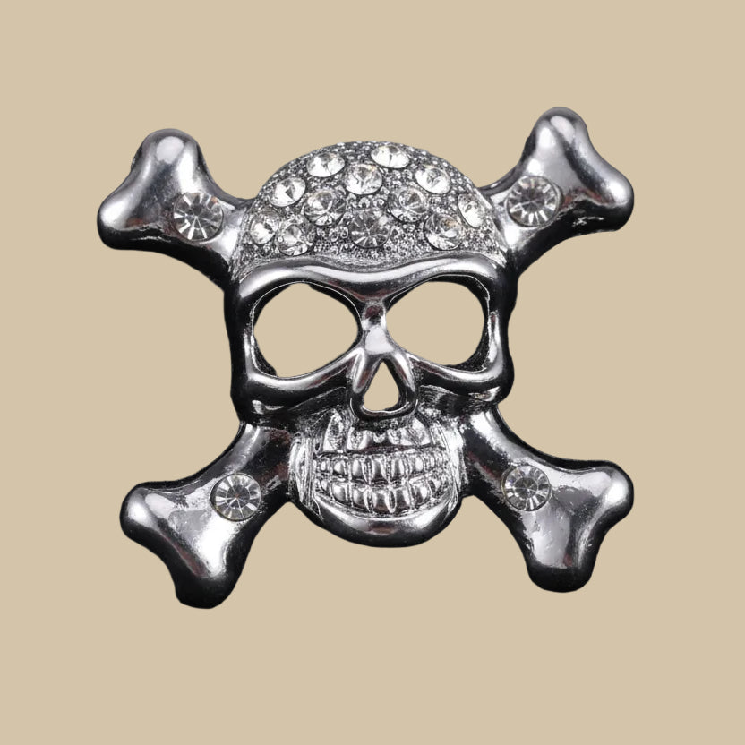Silver skull and crossbones brooch pin with clear crystal stones on a beige background
