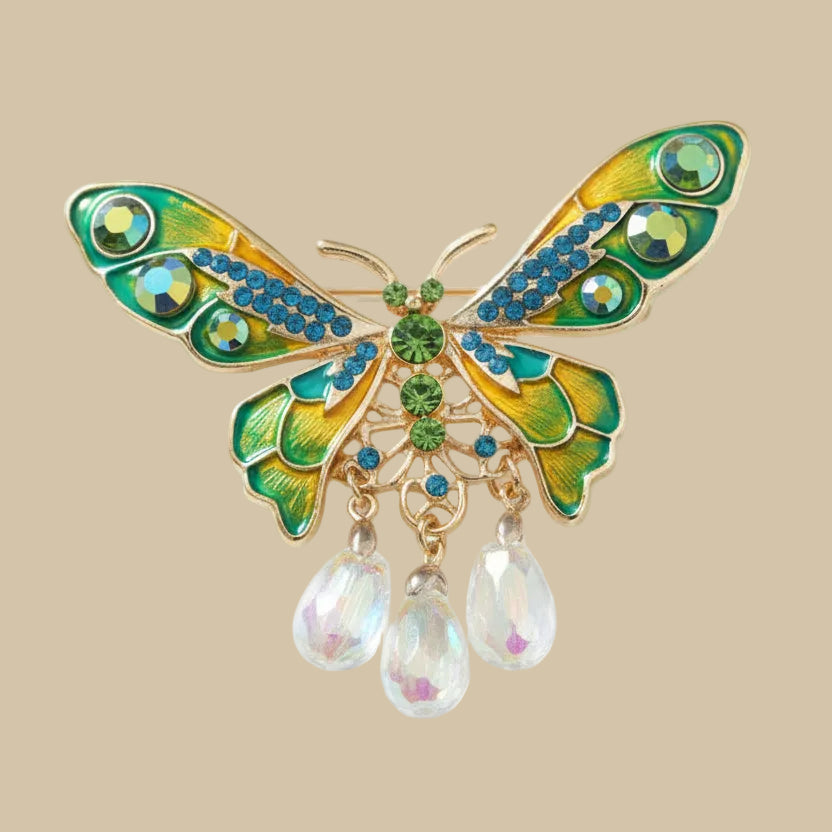 Whimsical style butterfly brooch with gemstones and dangling beads on a soft white background